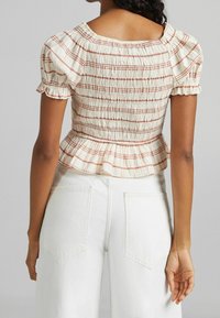 Top bianco smockato con strisce orizzontali marrone chiaro, maniche a sbuffo corte e orlo arricciato. Progettato con scollatura quadrata.