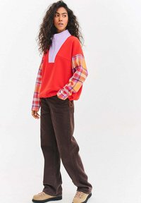 Czerwony i lawendowy półgolf z zamkiem, z rękawami w kratę, zestawiony z szerokimi, ciemnobrązowymi spodniami i beżowymi botkami na sznurowadła.