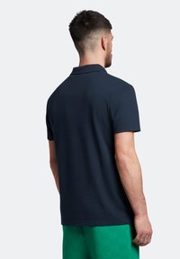 Polo shirt blu navy con colletto standard e maniche corte, realizzato in tessuto liscio; modello che indossa pantaloni corti a quadretti verdi.