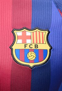 Το έμβλημα της ποδοσφαιρικής ομάδας FC Barcelona με κόκκινες και μπλε κάθετες ρίγες σε φόντο υφάσματος με ριμπ υφή.