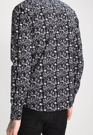 Zwart shirt met lange mouwen met een wit patroon van vintage elektronica, waaronder radio's, koptelefoons en cassette spelers, gedragen door een persoon die met de rug naar de kijker staat.