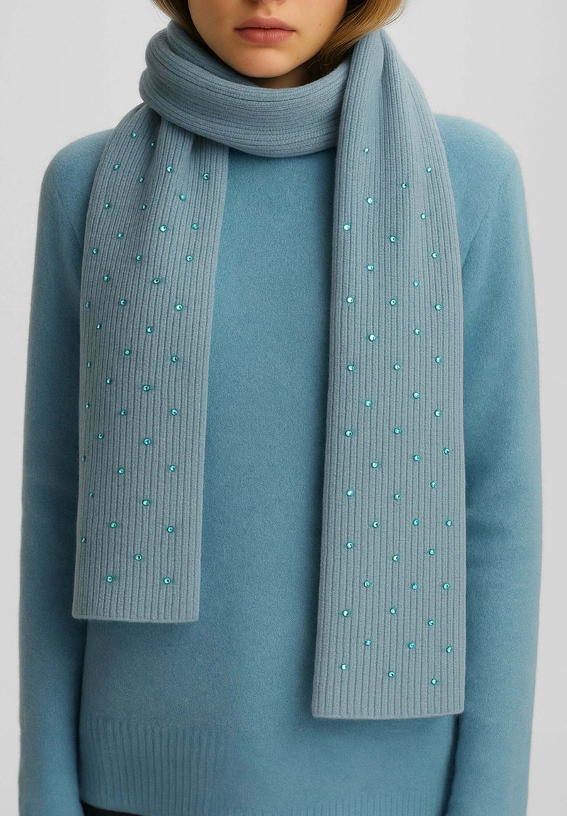 Sciarpa a coste di un blu chiaro con paillettes, realizzata in un morbido tessuto, avvolta attorno al collo; abbinata a un maglione blu coordinato.