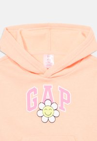 Felpa pesca con cappuccio e coulisse, caratterizzata dalla scritta "GAP" in rosa e da una grafica di una margherita sorridente sul davanti. Tessuto morbido e polsini a coste.