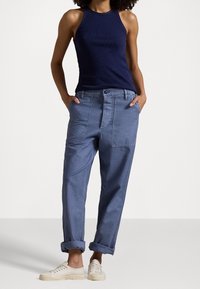 Haut halter en maille bleu marine associé à un pantalon cargo en denim bleu clair avec un bouton avant, des poches latérales et des ourlets retroussés. Baskets blanches décontractées.