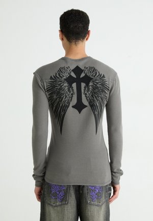Langärmliges graues Shirt mit gerippter Textur. Schwarzes Grafikdesign eines Kreuzes mit Flügeln auf dem Rücken. Einfacher Rundhalsausschnitt und taillierte Ärmel.