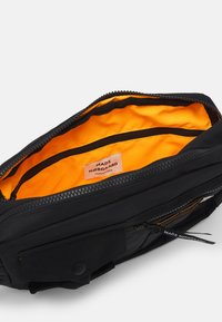 Black bag with a zipper closure; features an orange interior and a small label. Includes two zippered compartments and a buttoned flap.