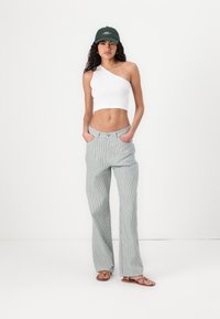 Witte geribbelde een-schouder crop top, gestreepte broek met brede pijpen in lichtblauw en wit, groene pet, bruine sandalen. Minimalistisch ontwerp en casual pasvorm.