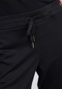 Svarta joggerbyxor med en teksturerad midja, snörning med metallspetsar och en slät tygytan.