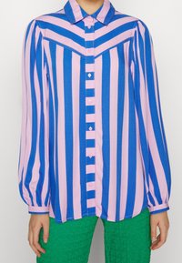 Chemise à manches longues rayée bleu et rose avec col, fermeture à boutons et tissu texturé ; présente des manches bouffantes et des accents contrastants.