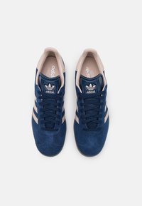 Adidas-sneakers med ovandel i marinblå mocka, rosa accenter, tre vita ränder och mörkblå skosnören. Textilfoder och gummisula.