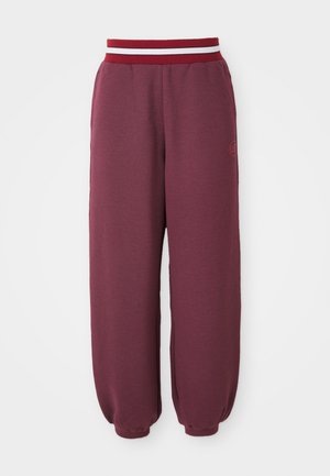 Pantalones joggers color burdeos con tejido texturizado, piernas ajustadas y una cinturilla a rayas en rojo y blanco que contrasta. Presenta un pequeño logo en el costado.