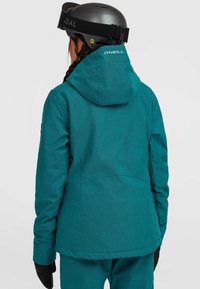 Teal sneeuwjack met een gestructureerde afwerking, verstelbare kap en zwarte accenten. Voorzien van een ritszak en logo op de achterkant.