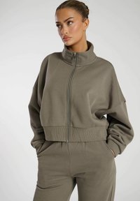 Olijfgroene cropped sweatshirt met hoge hals, voorrits, geribde zoom en verlaagde schouders. Glad materiaal met een ontspannen pasvorm.