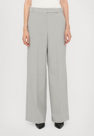 Nainen pukeutunut vaalean harmaisiin leveälahkeisiin housuihin, joissa on etuhelmat ja piilotettu vyötärönauhan suljin, yhdistettynä mustiin teräväkärkisiin kenkiin.