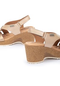 Sandalias con cuña que presentan un upper de piel beige con correas entrecruzadas, tacón de corcho y plantilla texturizada marrón. Incluyen una correa trasera ajustable.