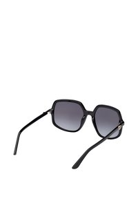 Zwarte zonnebril met een zeskantig montuur, graduele glazen en slanke pootjes. Voorzien van subtiele gouden accenten bij het scharnier.