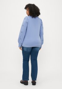 Απαλή μπλε πουλόβερ με φουσκωτά μανίκια και λεπτομέρειες από ματιές. Συνδυασμένο με σκούρες μπλε φλαρέ παντελόνες και καφέ πλατφόρμες μποτών.