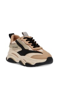 Baskets en maille beige avec des accents noirs, semelle en caoutchouc blanc épais et lacets proéminents. Comprend une languette en nylon grise et des détails texturés.