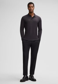 Szara, ciemnoszara koszulka polo z długim rękawem i kołnierzykiem, zestawiona z czarnymi spodniami i czarnymi sznurowanymi butami, na neutralnym szarym tle.