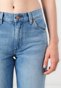 Jeans in denim blu chiaro con vita alta, dotati di chiusura con bottone, tasche anteriori e cuciture a vista. Texture liscia e vestibilità slim.