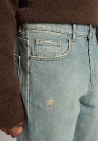 Ljusblå denimjeans med en blekt textur och ett litet slitage. I kombination med en brun stickad tröja som visar tygets värme.