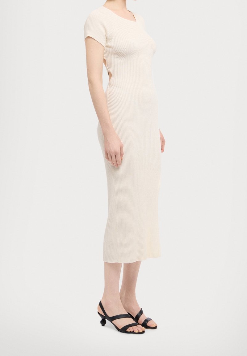 Geripptes Strickkleid in hellbeige mit quadratischem Ausschnitt und kurzen Ärmeln, kombiniert mit schwarzen Riemchensandalen mit abgerundeten Absätzen.