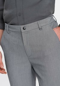 Grå byxor i texturerat tyg, med slät framtill, sidofickor och svart knappknäppning vid midjan.