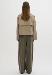 Beige kort jacka med knappstängning, med en avslappnad passform och ryggfickdetalj, ihop med vida olivgröna byxor i texturerat tyg.