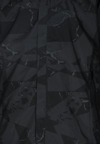 Giacca nera con un motivo geometrico in diverse sfumature di nero. Presenta una texture liscia, chiusura con zip e tasche laterali discrete.