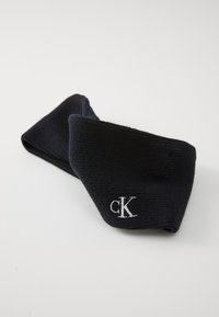 Zwarte geribbelde haarband met een zachte textuur, voorzien van een witte geborduurde "ck"-logo aan de voorkant.