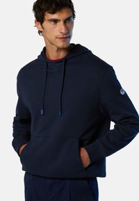 Marineblauer Hoodie aus weichem Stoff, mit einer vorderen Tasche, Kordeln mit blauen Spitzen und einem Logo auf dem linken Ärmel.