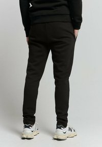 Zwarte joggings met een tapered fit, met een platte tailleband, twee achterzakken en gecombineerd met zwart-witte sport sneakers.