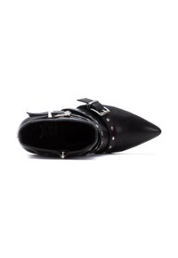 Botín de cuero negro hasta el tobillo con punta afilada, hebilla plateada y acentos de tachuelas, y forro interior texturizado. Presenta un diseño elegante.