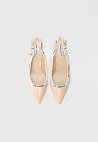 Bež čevlji s patentnim usnjem, koničastim prstom in slingback peto z belimi trakovi ter črnim logotipom. Gladek tekstura, elegantna zasnova.