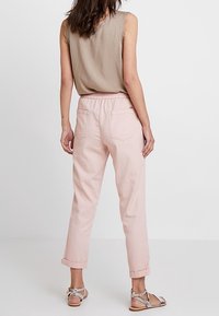 Světlé růžové, tapered kalhoty s volným střihem, které mají elastický pas, manžetové nohavice a dvě zadní kapsy. V kombinaci s béžovým topem.