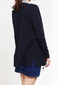 Maglietta a maniche lunghe blu navy con colletto a righe, spacchi laterali e vestibilità ampia, abbinata a una gonna di jeans. Morbido al tatto.