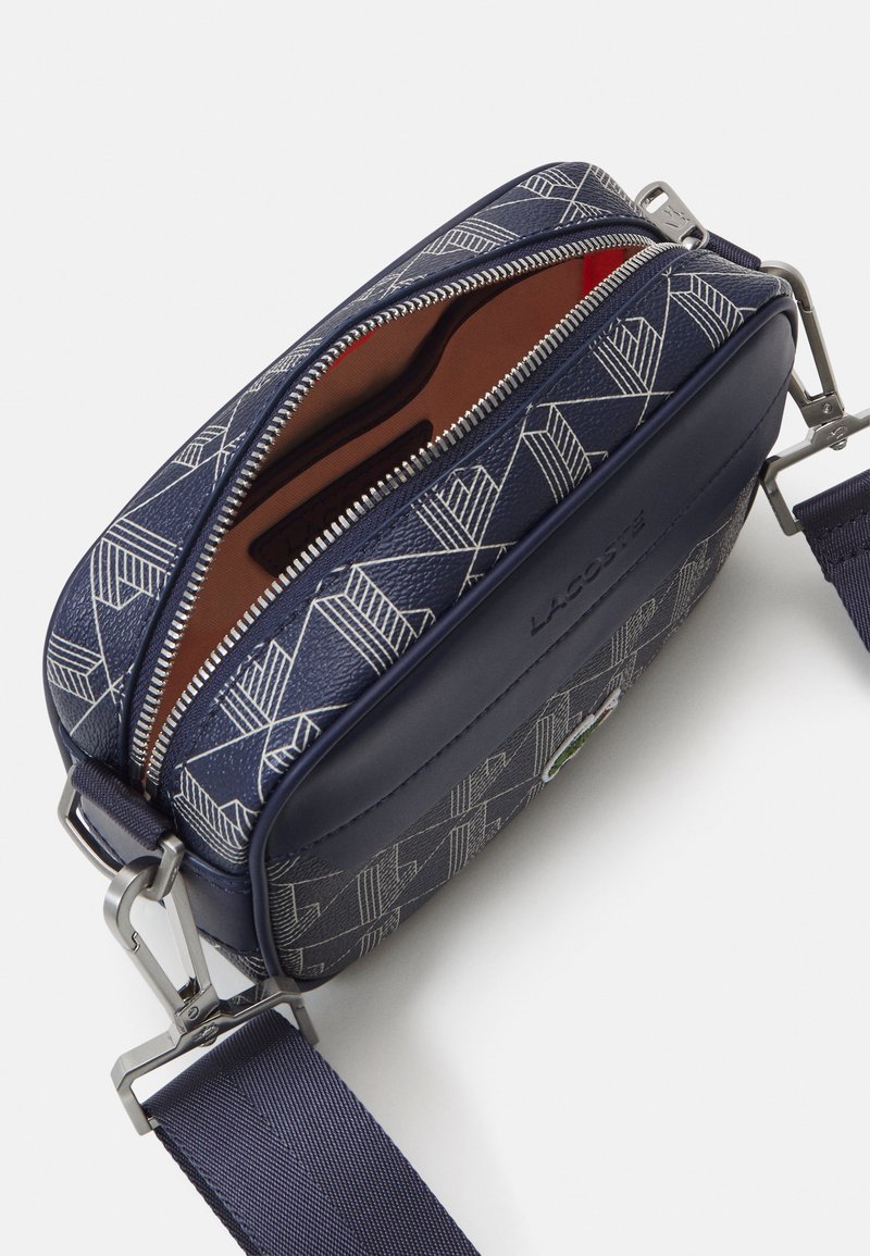 Sac à bandoulière marine avec motif géométrique, accents en cuir, fermeture éclair argentée et poche intérieure. Sangle en nylon réglable pour plus de commodité.