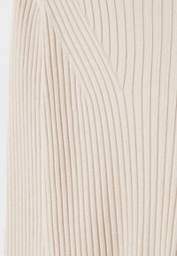 Beiger geripptes Gewebe mit vertikalen Linien, das eine strukturierte Oberfläche und einen subtilen Glanz aufweist. Details umfassen einen V-Ausschnitt.