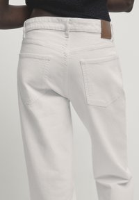 Jeans in denim bianco con una vestibilità rilassata, dotati di due tasche posteriori, una toppa in pelle marrone in vita e una texture liscia.