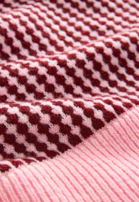Pletená textilie v burgundské a světle růžové barvě, která má kostkovaný vzor se střídajícími se barvami a ribbovanou texturu na okrajích.
