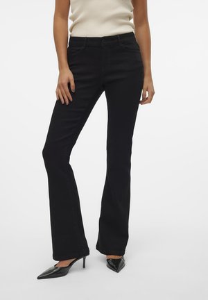 Jean noir évasé en denim, avec une taille mi-haute et des poches avant, associé à des talons aiguilles noirs. Texture lisse.