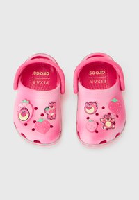 Zoccoli in gomma rosa con fori di ventilazione e spilli decorativi removibili a forma di orsetti e fragole. Superficie leggermente strutturata, design flessibile.