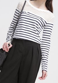 Långärmad topp med vita och marinblå horisontella ränder, detaljerad spetsbyxa, kombinerad med högmidjade svarta byxor och en läderväska.