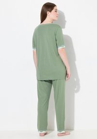 Twee-delige pyjama set in zachte groene stof. Top heeft korte mouwen met kantafwerking; de broek heeft een ontspannen pasvorm met bijpassende kantaccenten bij de manchetten.