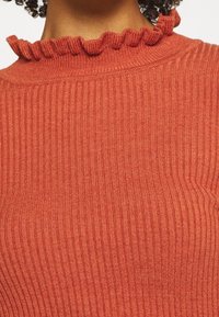 Prążkowany, rdzawego koloru sweter z wysokim kołnierzem, ozdobiony falbaną. Tekstura jest miękka i elastyczna, co podkreśla dopasowany krój.