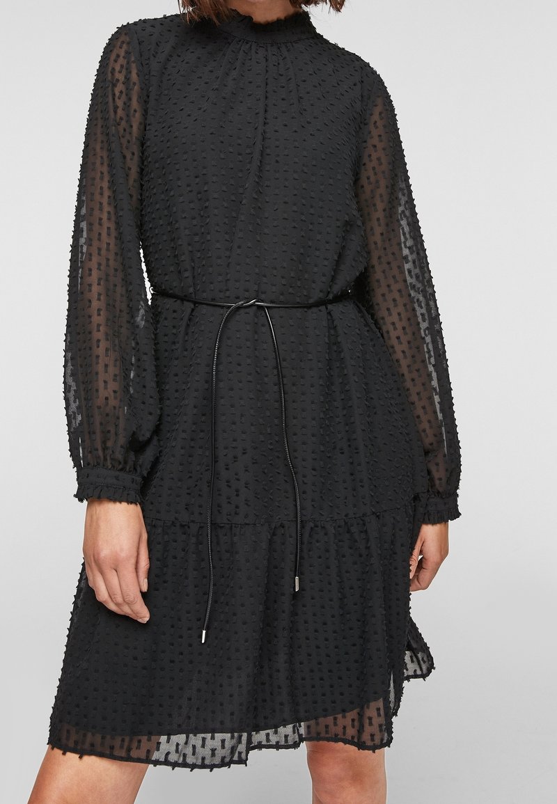 Black dress with sheer, textured fabric, long sleeves, gathered neckline, and a tied waist. Features a layered hem with ruffled edges.