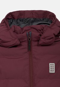 Burgundská zateplená bunda s vysokým límcem, předním zipem a šedou nášivkou s logem. Vnitřní podšívka v kontrastní tmavší barvě.