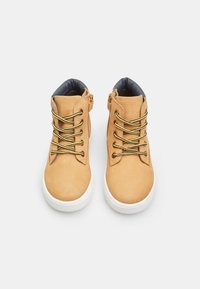 Zapatos altas de gamuza marrón con cordones dorados, suelas de goma blanca y un cuello acolchado en color azul marino. Presenta cremalleras laterales para facilitar su uso.
