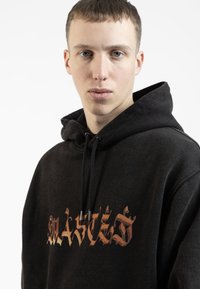 Čierna mikina s kapucňou vpredu so grafikou, na ktorej je napísané "WASTED" ozdobným zlatým písmom. Obsahuje kapucňu na šnúrky a mäkký povrch.