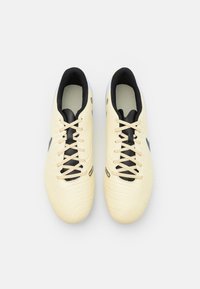 Light cream soccer shoes feature a textured upper, black laces, and a smooth black interior. The design includes a subtle logo on the sides.
